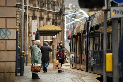 Los viajeros usan tapabocas mientras esperan en una parada de tranvía en Sheffield, South Yorkshire, el 21 de octubre de 2020, antes de que entren en vigor nuevas medidas de bloqueo a medida que aumenta el número de casos de coronavirus