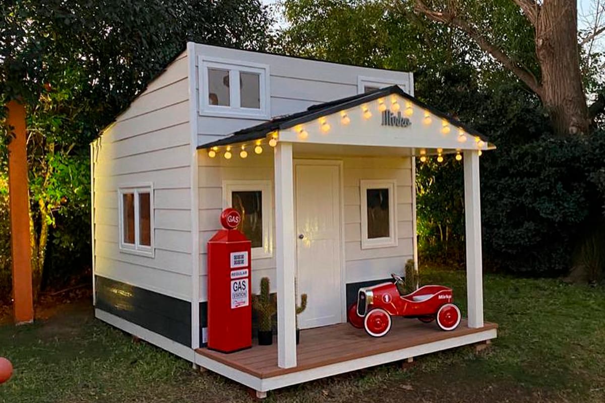 Luces, una galería con dos columnas, un auto y un surtidor de juguete decoran el exterior de la casa de madera que el conductor le regaló a su hijo