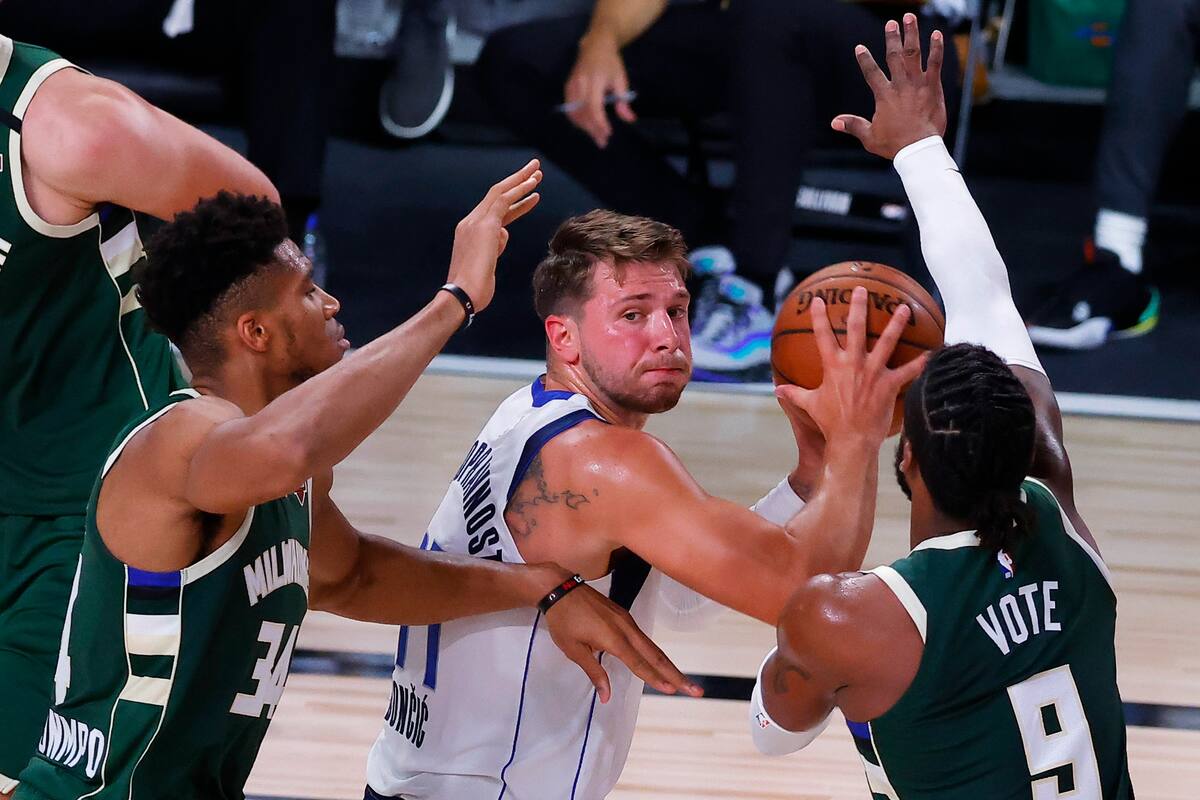 Luka Doncic de los Dallas Mavericks, en el centro, busca pasar el balón mientras Giannis Antetokounmpo de Milwaukee Bucks, a la izquierda, y Wesley Matthews defienden durante un juego de baloncesto de la NBA el sábado 8 de agosto de 2020 en Lake Buena Vista, Florida