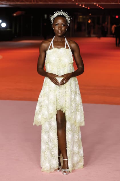 Lupita Nyong’o brilló con un etéreo traje blanco y amarillo de la colección Alta Costura primavera/verano 2022 de Chanel con estampado floral y detalles de volados, que combinó con sandalias doradas, joyas De Beers y un tocado floral.