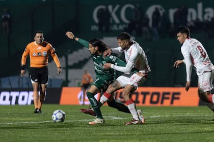 Magnín aguanta la pelota ante la marca de Godoy; sigue la acción de cerca del árbitro Lobo Medina