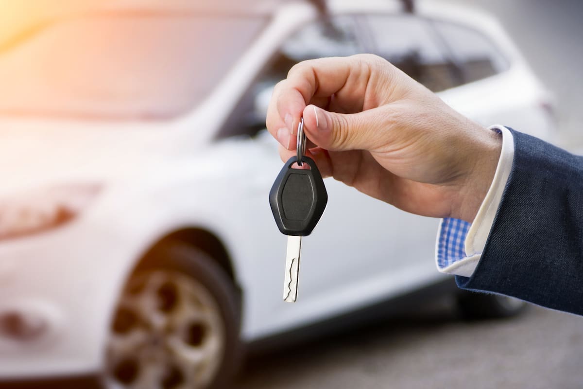Male holding car keys with car on background