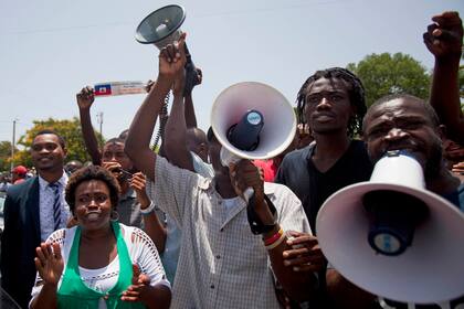 Manifestantes corean consignas contra Francia mientras el presidente francés Francois Hollande pronuncia un discurso frente al Palacio Nacional en Puerto Príncipe, Haití, el 12 de mayo de 2015. (AP Foto/Dieu Nalio Chery, File)