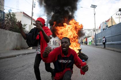 Manifestantes gritan consignas contra el gobierno frente a una barricada de neumáticos en llamas durante una protesta, el viernes 18 de noviembre de 2022, en Puerto Príncipe, Haití. (AP Foto/Odelyn Joseph)