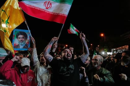 Manifestantes iraníes corean eslóganes mientras ondean banderas nacionales y exhiben fotos del líder supremo