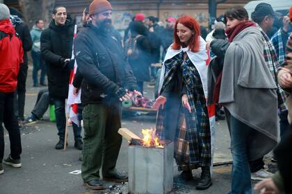 Manifestantes se calientan en una hoguera durante una protesta contra los resultados de las elecciones parlamentarias en Tiflis, Georgia, el 18 de noviembre de 2024. (AP Foto/Zurab Tsertsvadze)