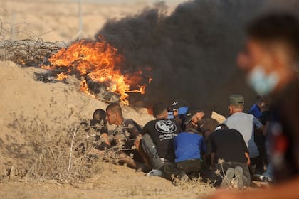 Manifestantes se protegen cerca de neumáticos en llamas en las inmediaciones de la cerca fronteriza entre Gaza e Israel durante una protesta, al este de Khan Younis, en el sur de la Franja de Gaza, el 25 de agosto de 2021. (AP Foto/Abdel Kareem Hana)