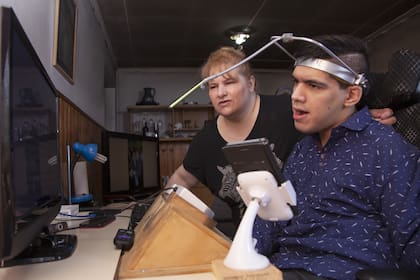 Manu Gutiérrez, de 25 años, junto a su mamá; para escribir en la computadora usa un dispositivo especial.