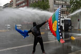 Un hombre con una bandera mapuche se enfrenta a la policía durante una protesta en Santiago de Chile