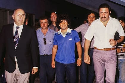 Maradona sonríe por los pasillos de la Bombonera, mientras camina rumbo a la sala donde firmará el contrato para las cámaras. A su izquierda, Rubén Dodero, de camisa blanca y bigotes, lo escolta