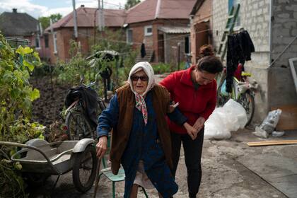 Mariia Ruban, de 92 años, recibe ayuda de una vecina para caminar por el jardín de su casa, que sufrió daños en el tejado y las ventanas tras un ataque ruso, en Sloviansk, Ucrania, el 6 de septiembre de 2022. (AP Foto/Leo Correa)