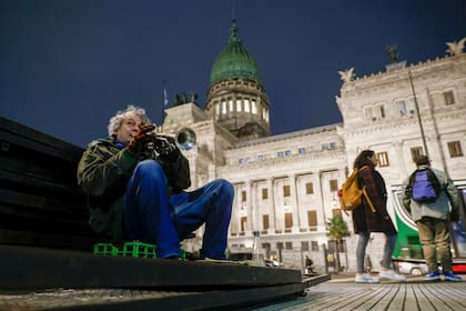 Mario toca la trompeta a la gorra sentado sobre las vallas policiales que depositaron para la sesión de hoy por la ley de tierras.