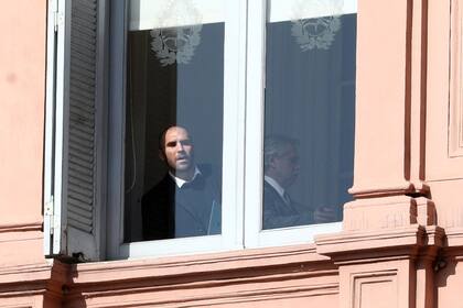 Martín Guzmán se asoma desde una ventana de la Casa Rosada, al lado está Alberto Fernández, antes del anuncio por el cambio en ganancias