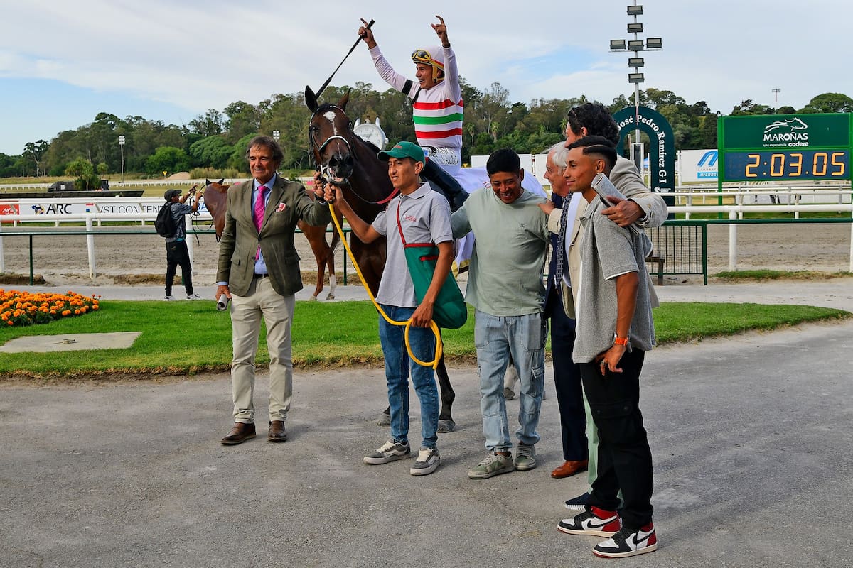 Martín Valle celebra en la montura de Martana, la ganadora del Ciudad de Montevideo (G1), rodeada de parte del equipo de Enrique Martín Ferro (izq.), en Maroñas.