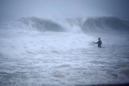 Matt Prue, de Stonington, Connecticut, camina en el Océano Atlántico para surfear las olas de la tormenta tropical Henri mientras el sistema se aproximaba, en Rhode Island, el domingo 22 de agosto de 2021. (AP Foto/Stew Milne)