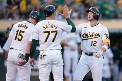 Max Schuemann (12), de los Atléticos de Oakland, celebra después de conectar jonrón de tres carreras, jugada en la que anotaron también Seth Brown (15) y Brett Harris (77) durante la cuarta entrada del juego de béisbol en los Angelinos de Los Ángeles en Oakland, California, el viernes 19 de julio de 2024. (AP Foto/Jeff Chiu)