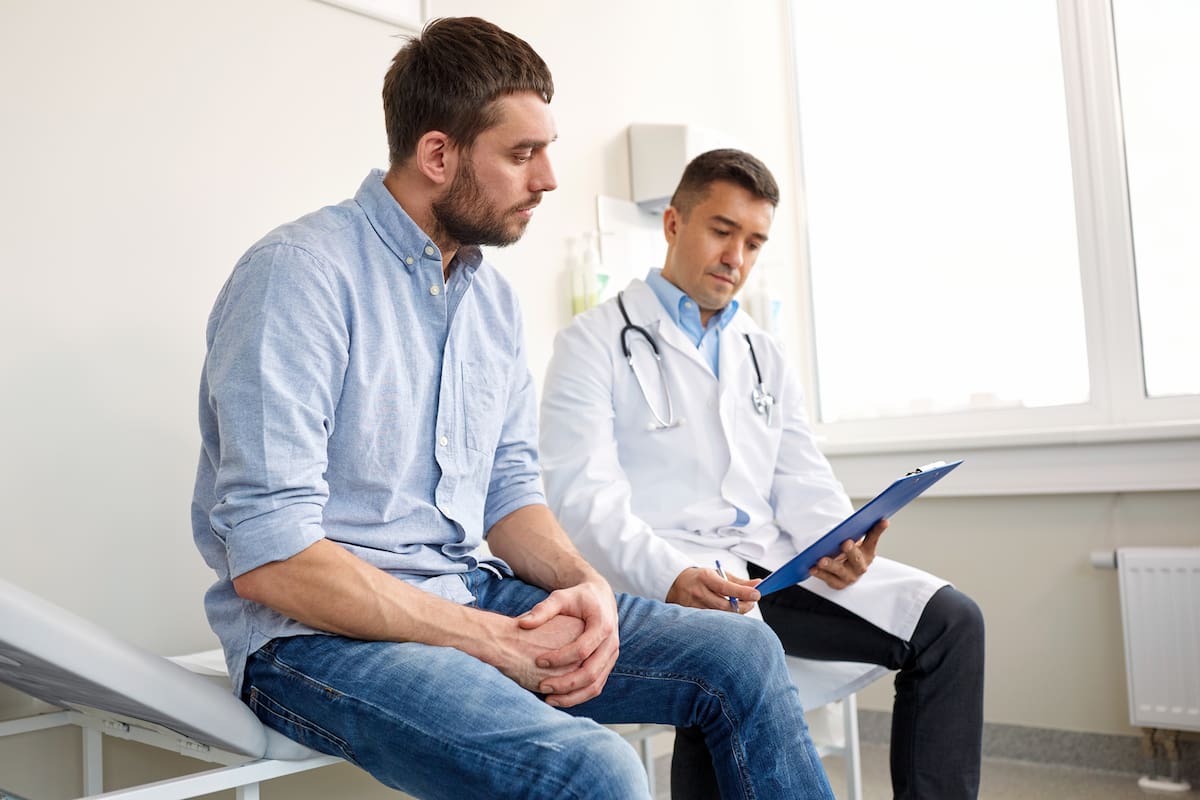 medicine, healthcare and people concept - doctor with clipboard and young male patient having health problem meeting at hospital