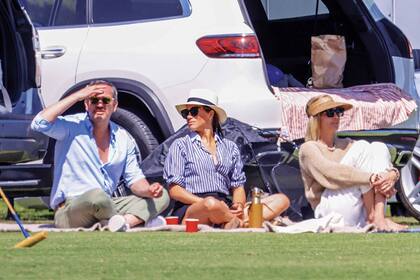 Meghan Markle y Delfina Blaquier miran juntas el partido, sentadas sobre unas lonas.