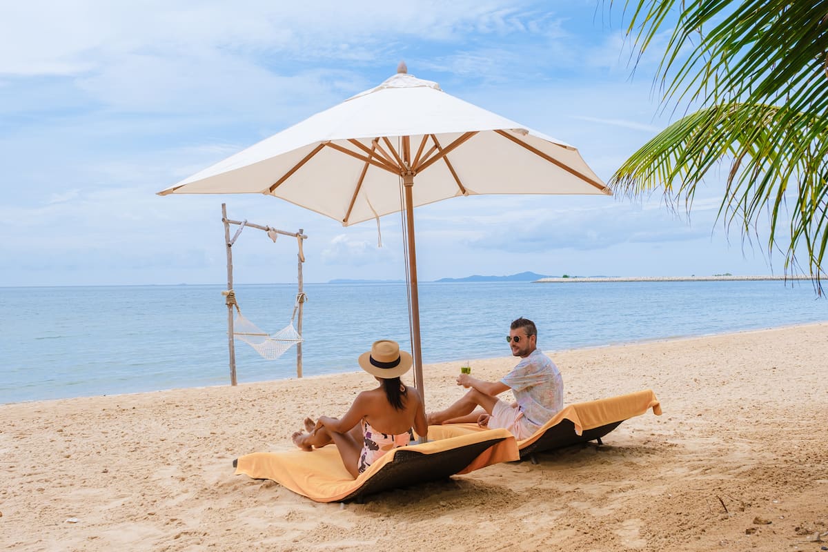 Men and women on the beach are relaxing in a beach chair on a sunny day with a hammock in Pattaya Thailand Ban Amphur beach. couple walking on a tropical beach with palm trees and hammock