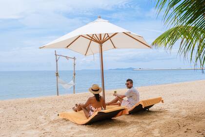 Men and women on the beach are relaxing in a beach chair on a sunny day with a hammock in Pattaya Thailand Ban Amphur beach. couple walking on a tropical beach with palm trees and hammock