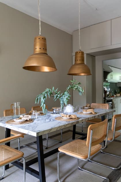 Mesa con tapa de Neolith (De Mori Mármoles), sillas (Landmark), alfombra (Mihran). Vajilla de cerámica (Hábitat Home), servilleteros (H&M Home), servilletas y vasos (Binah Deco). Lámparas galponeras pintadas en dorado y bronce.