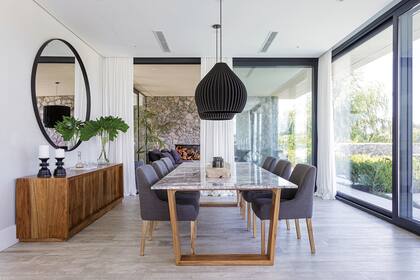 Mesa de comedor ‘Lyla’ con tapa de mármol y estructura en madera, sillas ‘Roma’ tapizadas, vajillero de petiribí y lámparas colgantes ‘3D’ (todo de Negro House Pleasures).