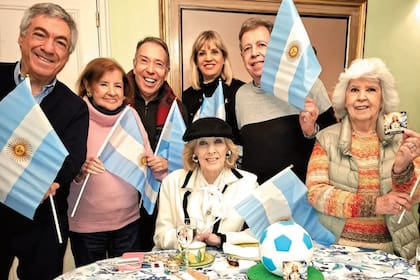 Mesa temática: en tiempos del último Mundial, con torta de pelota de fútbol y estampitas de “Santa Mirtha”, que se volvieron virales. De izquierda a derecha, Dany Mañas, María Teresa Villaroel, Alejandro Veroutis, Teté Coustarot, Héctor Vidal Rivas y Amalia Idoyaga Molina rodean a la anfitriona