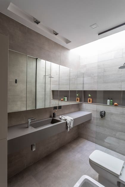 Mesada con bacha integrada de Neolith ‘Cement Satin’ (Marmolería Gaona) y grifería monocomando (FV). Sanitarios (Ferrum). Piso y revestimiento de pared unificados (SBG)
