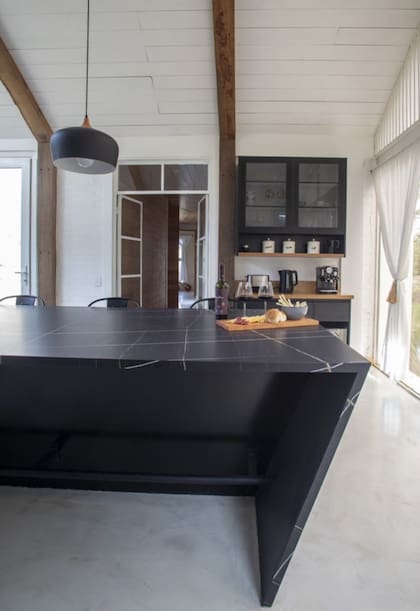 Mesada, estantes de lenga y muebles de MDF negro (todo, arquitecto Tulio Rossini). Los troncos de roble pellín interrumpen el blanco y subrayan el perfil del techo a dos aguas.