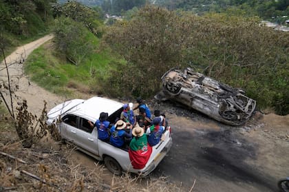 Miembros de la Guardia Indígena pasan junto a un vehículo que quemaron después de un ataque de rebeldes del Estado Mayor Central en Toribío, Colombia, el martes 19 de marzo de 2024. (AP Foto/Fernando Vergara)