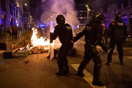 Miembros de la policía regional catalana Mossos dEsquadra toman posición junto a la basura en llamas incendiada por los manifestantes durante una protesta contra las nuevas restricciones del coronavirus en Barcelona el 30 de octubre de 2020