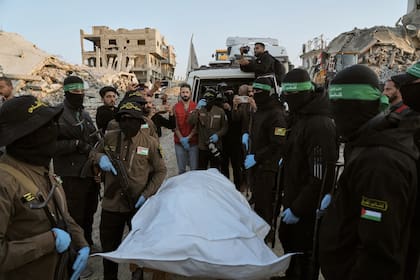 Miembros de los grupos Yihad Islámica y Hamás, con el rostro enmascarado, entregan una bolsa que se cree que contiene los restos de un rehén fallecido a la Cruz Roja, para su traspaso a las autoridades israelíes, en Beit Lahiya, en el norte de la Franja de Gaza, el 3 de diciembre de 2025. (AP Foto/Jehad Alshrafi)