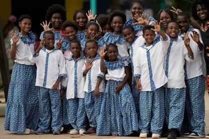 Miembros de un coro de niños saludan a los periodistas mientras esperan la llegada del príncipe Harry y Meghan, en San Basilio de Palenque, Colombia, el sábado 17 de agosto de 2024. (Foto AP/Iván Valencia)