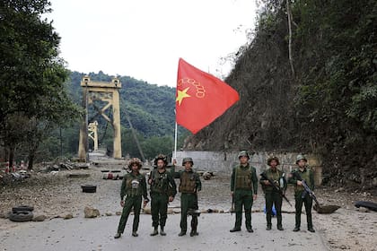 Miembros del Ejército de la Alianza Democrática Nacional de Myanmar posan para una fotografía con la bandera del grupo frente al puente de Kunlong, en el municipio de Kunlong, estado de Shan, Myanmar, domingo 12 de noviembre de 2023. (El medio de comunicación en línea Kokang vía AP).