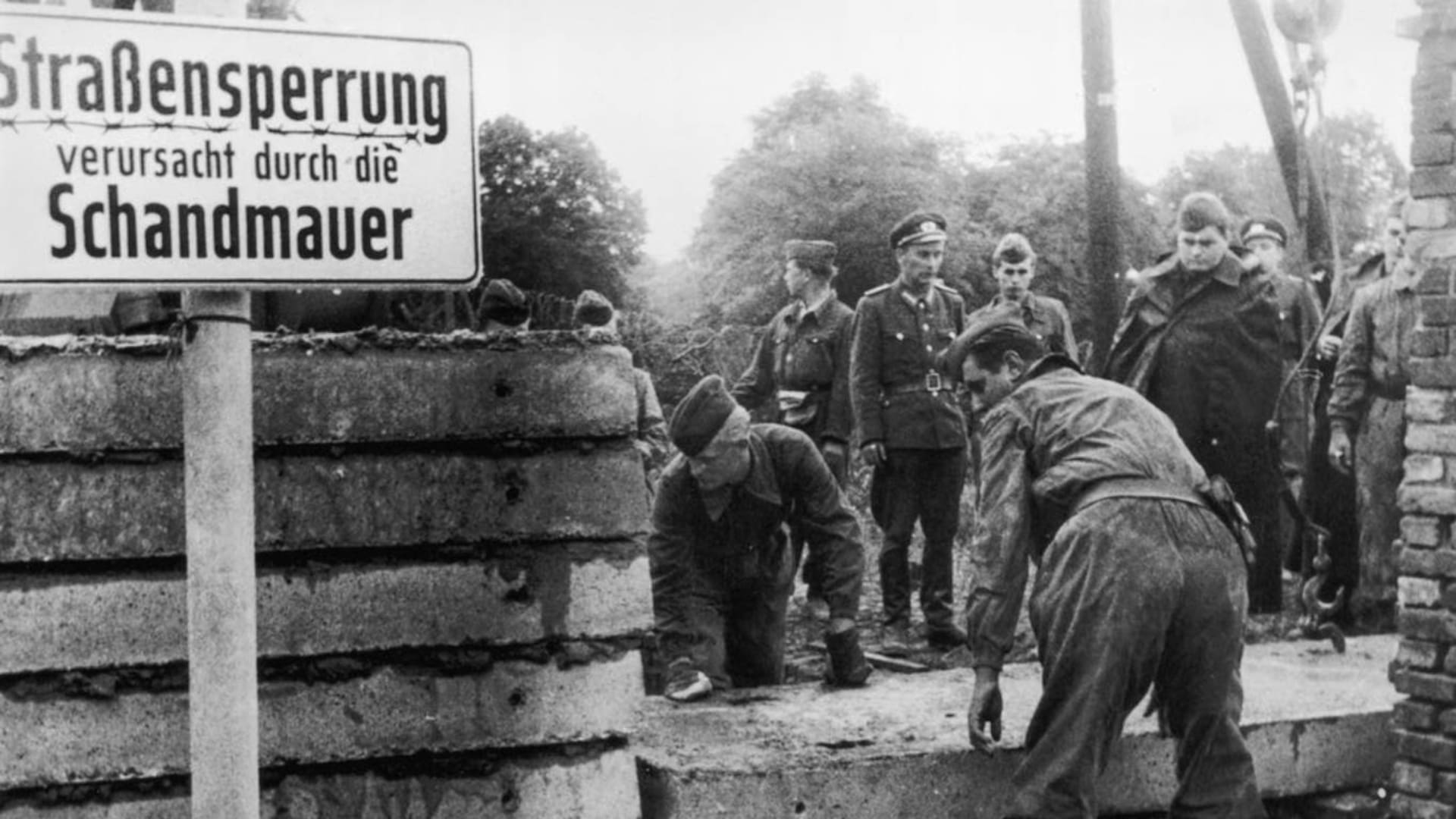 Mientras los agentes de la República Democrática Alemana levantan su muro, un cartel del lado occidental presenta una queja: "Straßensperrung verursacht durch die Schandmauer" ("Cierre de calle causado por el muro de la vergüenza")