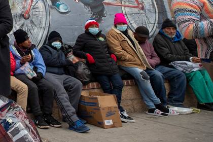 Migrantes comen y esperan ayuda, acampados en una calle del centro de El Paso, Texas, 18 de diciembre de 2022.  (AP Foto/Andres Leighton)