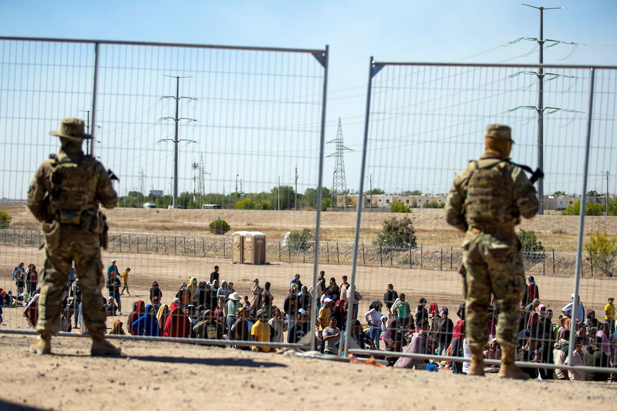 Migrantes esperan en una fila junto a una valla fronteriza mientras miembros de la Guardia Nacional de Texas los vigilan, en El Paso, Texas, el 10 de mayo de 2023. (AP Foto/Andres Leighton, Archivo)