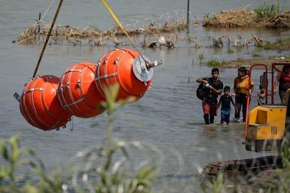 Migrantes observan unas boyas grandes utilizadas como valla fronteriza en el río Bravo, a la altura de Eagle Pass, Texas (AP Foto/Eric Gay)