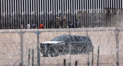 Migrantes que buscan asilo en Estados Unidos son vigilados por agentes de Texas junto al muro fronterizo en El Paso