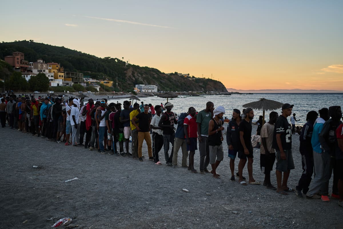 Migrantes que cruzaron desde Marruecos a España hacen fila para recibir comida en una playa en el te