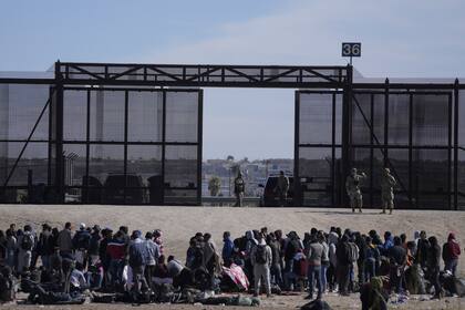 Migrantes que cruzaron la frontera desde México hacia Estados Unidos esperan a un costado del muro fronterizo en donde agentes de la Patrulla Fronteriza de Estados Unidos montan guardia, el 30 de marzo de 2023 (Archivo)