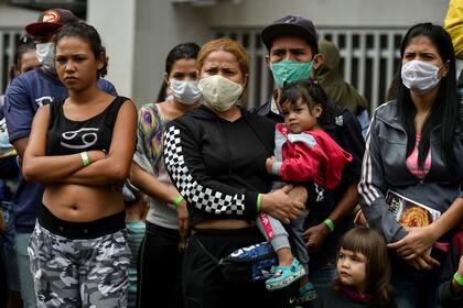Migrantes venezolanos esperan el autobús para regresar a su país desde Colombia con barbijos para protegerse del coronavirus