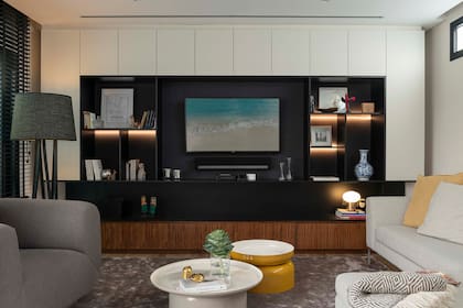 MTD Arquitectura diseñó un mueble de madera laqueada en blanco, con base en enchapado de nogal, estantes en negro con tiras led y centro entelado para mejorar la acústica de la TV. Lámpara de pie ‘Trigono’ y mesas bajas ‘Pluvial’ (Federico Churba). Sillón individual ‘Masa’ (Federico Varone para Adelphi) y sofá en L diseñado por el Estudio.