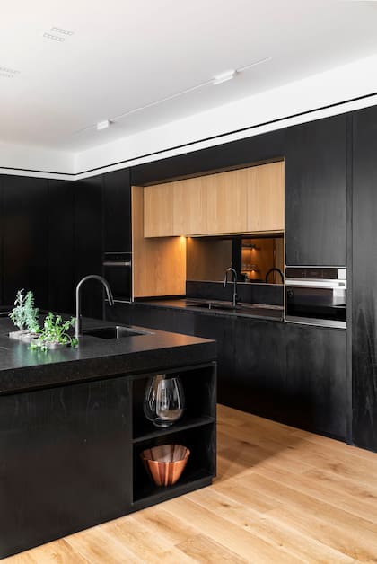 Mueble de cocina (Radovic Arquitecto, por Woodhead Studio) de MDF enchapado en paraíso de poro abierto laqueado y MDF enchapado en roble americano. Las mesadas son de granito ‘Negro Brasil’ leather (Marmolería Iarlori). Todo el piso del área social (The Flooring Company) es de roble de Eslavonia.