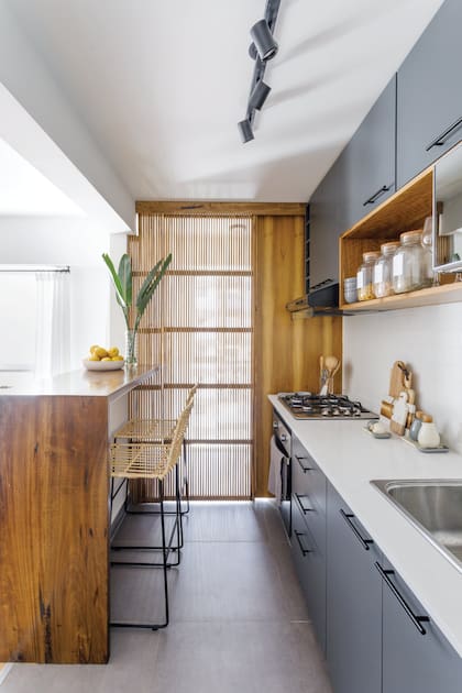 Muebles de cocina de MDF enchapado en melamina gris grafito y cajón revestido en madera de laurel (BT Construcciones), mesada de mármol ‘Venatino’ (Purastone). Barra de laurel (BT Construcciones) con dos banquetas (Philippa Deco Boutique)
