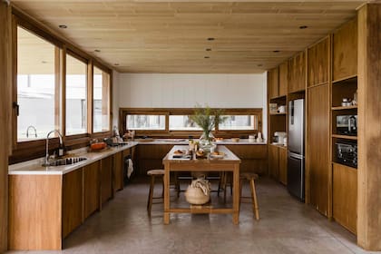 Muebles de cocina de petiribí natural (Talleres Sustentables). Mesadas de Dekton. El revestimiento blanco está hecho con tableros de MDF pintados. Sobre la isla, florero (Cari Ríos); debajo, canasto (Easy).