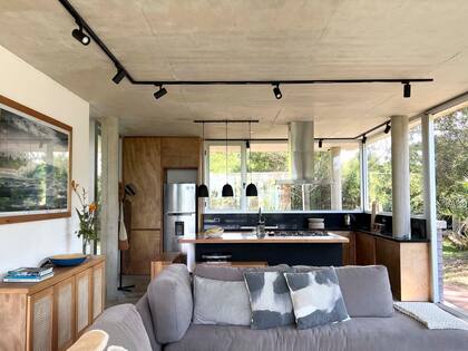 Muebles de cocina (diseño de Lago Project ejecutado por un carpintero de Rocha). Uno de los módulos se hizo hasta el techo para rodear la heladera con terminación gris acero. Pusieron el anafe para que tuviera vista al mar. La isla y los bancos que la acompañan tienen la altura calculada para ser mesa de comedor.