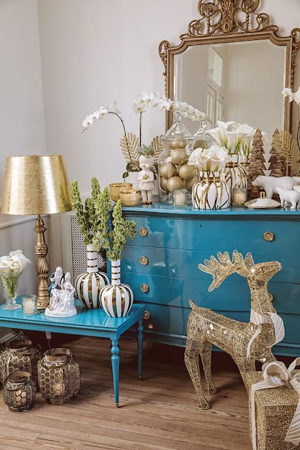 Muebles intervenidos y laqueados en azul calma con floreros en porcelana blanca y dorada, y osos polares blancos de Muy Arzuaga. Renos metálicos dorados de SheShu