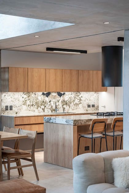 Muebles (Woodhead) en melamina 'Hickory' (Egger) con tiradores y bordes de kiri teñido. Mesada de cuarcita (Forte Dei Marmi). Anafe (Whirlpool) bajo un extractor cilíndrico (Maraldi).
