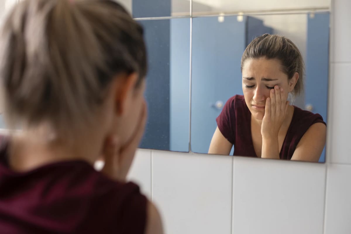 Mujer llorando frente a un espejo.